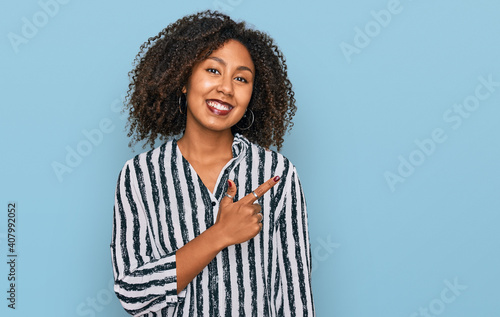 Young african american girl wearing casual clothes cheerful with a smile of face pointing with hand and finger up to the side with happy and natural expression on face © Krakenimages.com