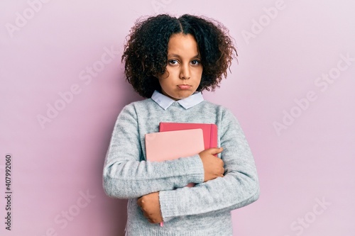Young little girl with afro hair holding books depressed and worry for distress, crying angry and afraid. sad expression.