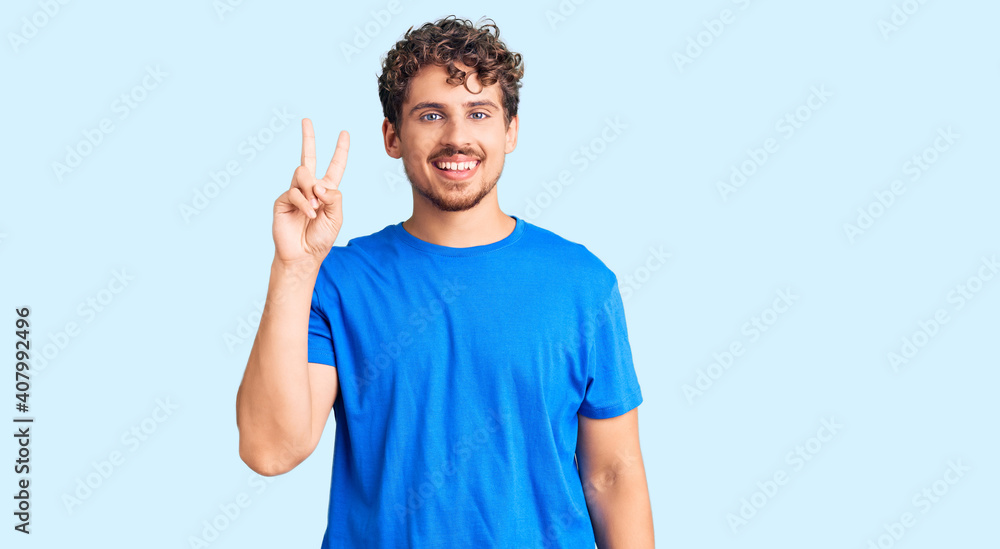 Young handsome man with curly hair wearing casual clothes showing and pointing up with fingers number two while smiling confident and happy. Young handsome man with curly hair wearing casual clothes showing and pointing up with fingers number two while smiling confident and happy.