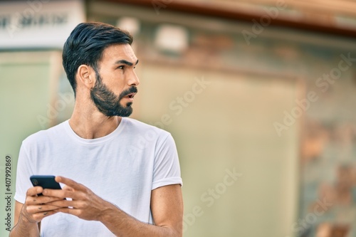 Young hispanic man with serious expression using smartphone at the city.