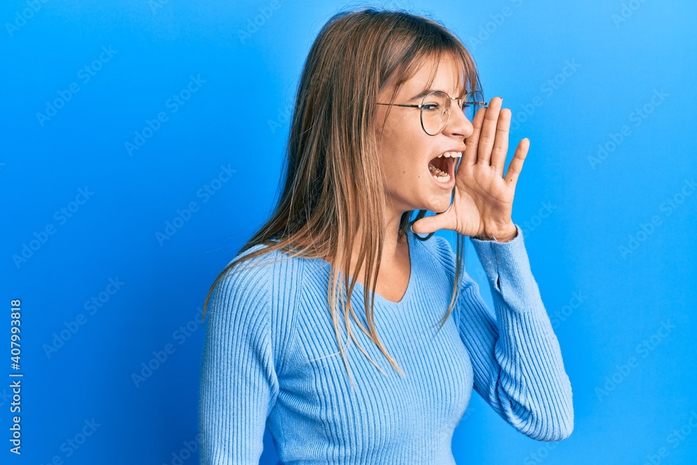 Teenager caucasian girl wearing casual clothes and glasses shouting and screaming loud to side with hand on mouth. communication concept. Teenager caucasian girl wearing casual clothes and glasses shouting and screaming loud to side with hand on mouth. communication concept.