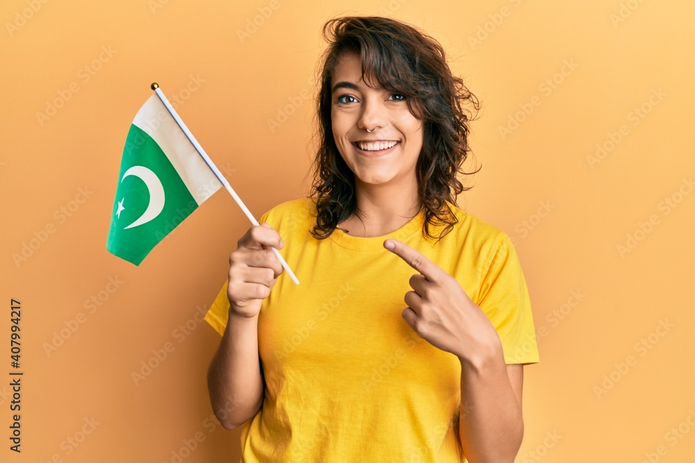 Young hispanic woman holding pakistan flag smiling happy pointing with hand and finger Young hispanic woman holding pakistan flag smiling happy pointing with hand and finger