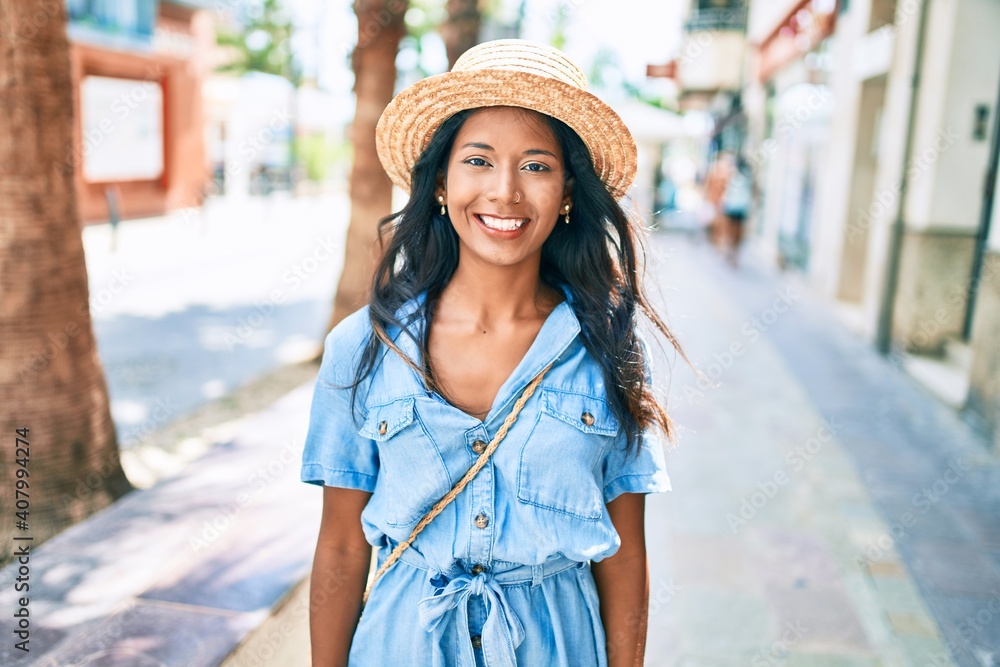 Young beautiful indian woman wearing summer hat smiling happy walking at the city.