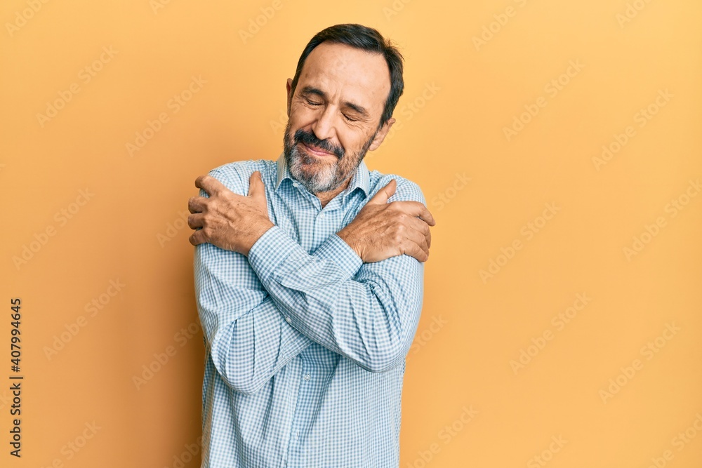 Middle age hispanic man wearing casual clothes hugging oneself happy and positive, smiling confident. self love and self care