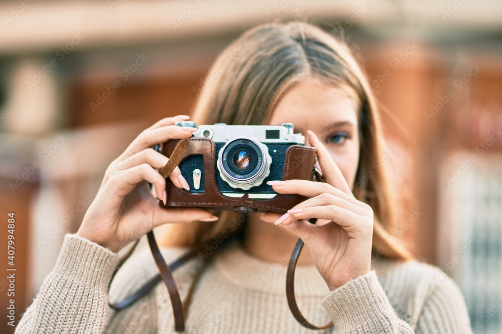 Beautiful caucasian teenager smiling happy using vintage camera at the city.