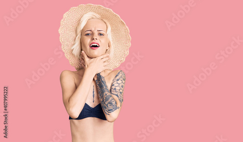 Young blonde woman with tattoo wearing bikini and summer hat shouting and suffocate because painful strangle. health problem. asphyxiate and suicide concept.