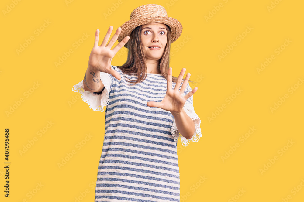 Beautiful caucasian woman wearing summer hat afraid and terrified with fear expression stop gesture with hands, shouting in shock. panic concept. Beautiful caucasian woman wearing summer hat afraid and terrified with fear expression stop gesture with hands, shouting in shock. panic concept.