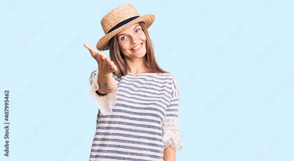 Fototapeta premium Beautiful caucasian woman wearing summer hat smiling friendly offering handshake as greeting and welcoming. successful business.