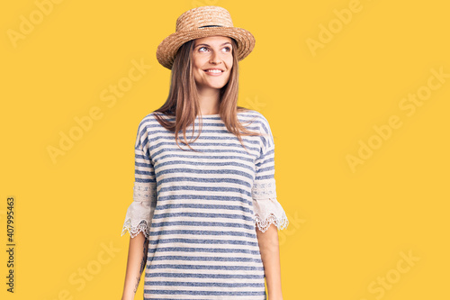 Beautiful caucasian woman wearing summer hat looking away to side with smile on face, natural expression. laughing confident.