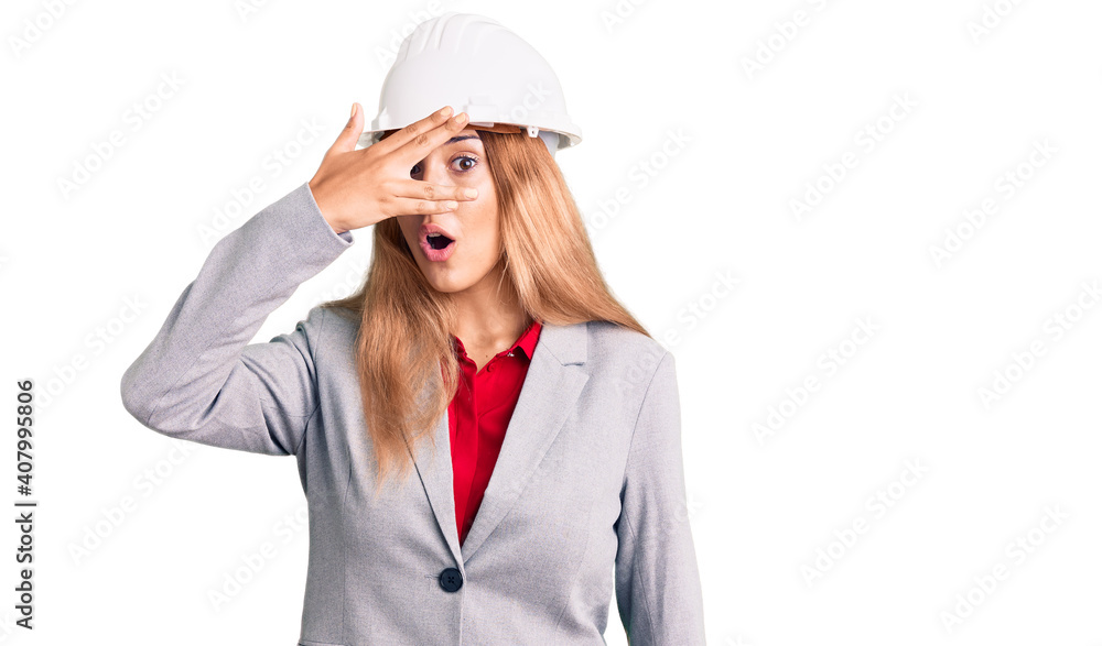 Beautiful young woman wearing architect hardhat peeking in shock covering face and eyes with hand, looking through fingers with embarrassed expression. Beautiful young woman wearing architect hardhat peeking in shock covering face and eyes with hand, looking through fingers with embarrassed expression.