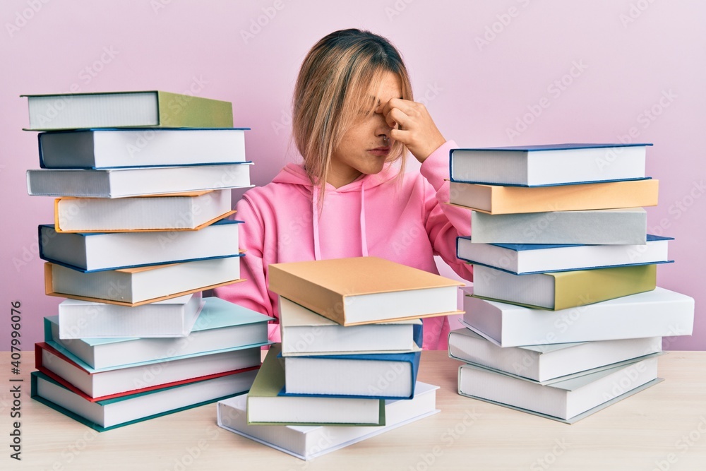 Young caucasian woman sitting on the table with books tired rubbing nose and eyes feeling fatigue and headache. stress and frustration concept. Young caucasian woman sitting on the table with books tired rubbing nose and eyes feeling fatigue and headache. stress and frustration concept.