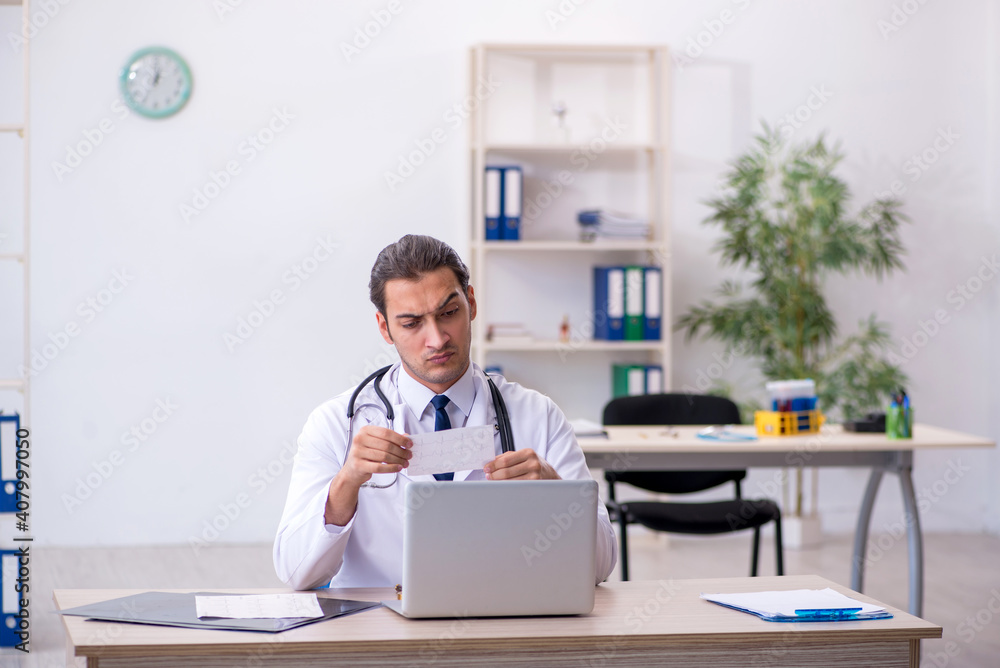 Young male doctor looking electrocardiogram in the clinic Young male doctor looking electrocardiogram in the clinic