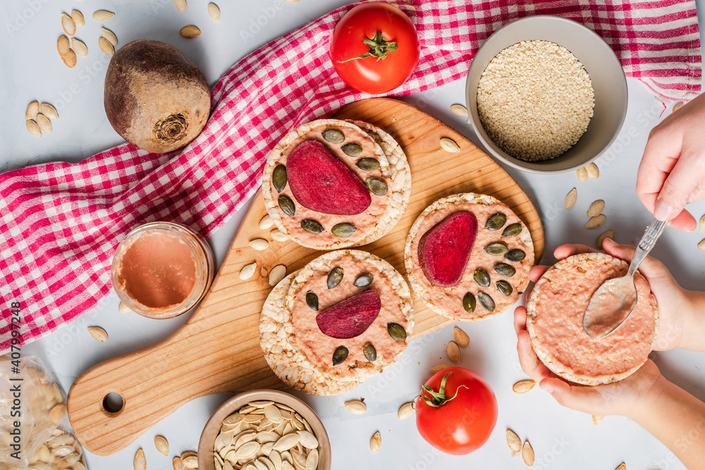 Crispy puffed rice cakes on table hummus spread and tomato and beet vegetables and sesame pumpkin seeds on the table - top view on hands preparing healthy vegetarian or vegan breakfast gluten free Crispy puffed rice cakes on table hummus spread and tomato and beet vegetables and sesame pumpkin seeds on the table - top view on hands preparing healthy vegetarian or vegan breakfast gluten free