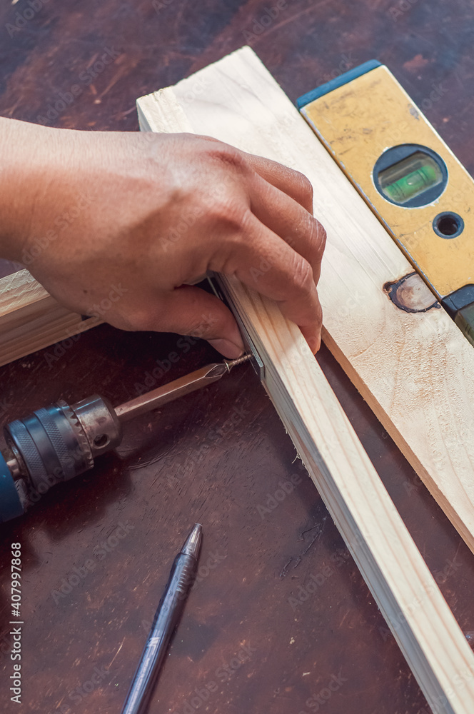 Woodworking with a drill to screw angle bracket in a wooden block with wood shavings and smoke in a woodworking workshop close-up power tool Woodworking with a drill to screw angle bracket in a wooden block with wood shavings and smoke in a woodworking workshop close-up power tool