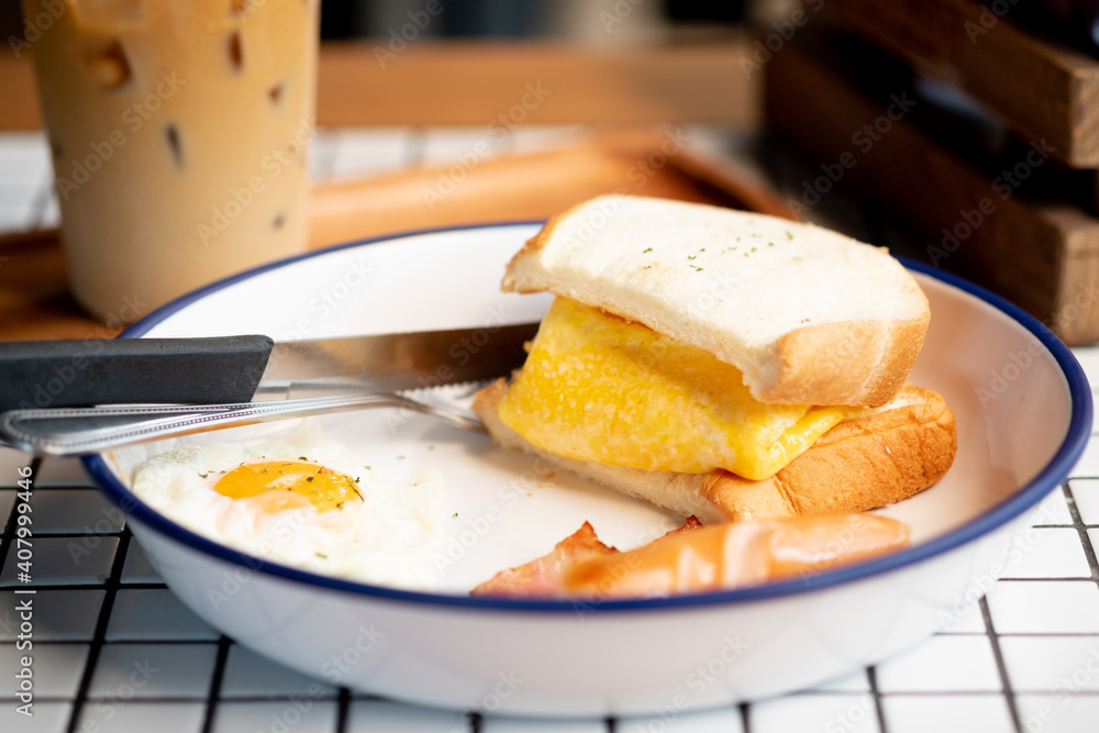 Fototapeta premium Egg in sandwich, sausage and bacon served with iced coffee.