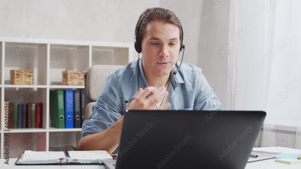 Workplace of freelancer. Employee works at home office using computer and headset. Young man is having a conference call. Remote job concept. Workplace of freelancer. Employee works at home office using computer and headset. Young man is having a conference call. Remote job concept.
