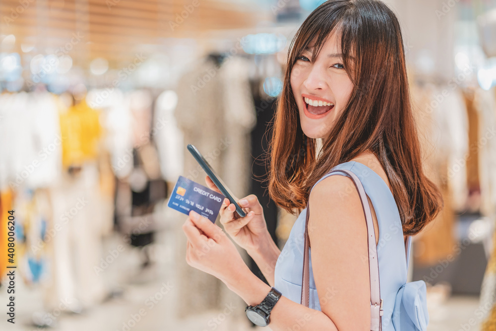Asian woman using credit card with mobile phone for online shopping in department store over the clothes shop store background, technology money wallet and online payment concept, credit card mockup