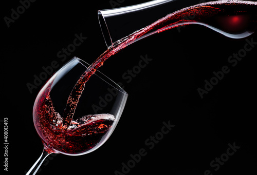 Red wine is poured into a wine glass on a black background.