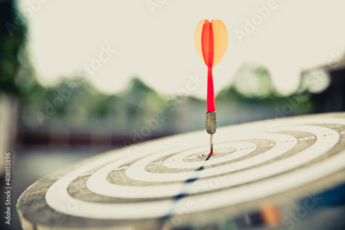 Close-up the bullseye target or dart board has red dart arrow throw hitting the center of a shooting with the sun shines and shadows for business targeting and winning goals business concepts