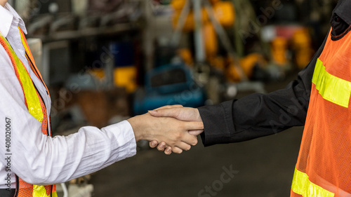 Two female factory workers or mechanical engineers in safety uniform check hand and make an agreement in a manufactory warehouse