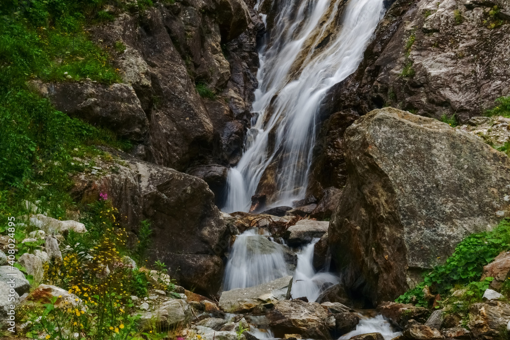 waterfall between rocks with flowers and plants on the side