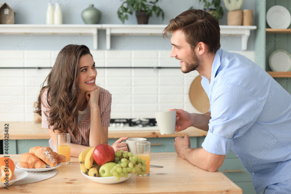 Beautiful young couple in pajamas is looking at each other and smiling  while cooking in kitchen at home. Stock Photo
