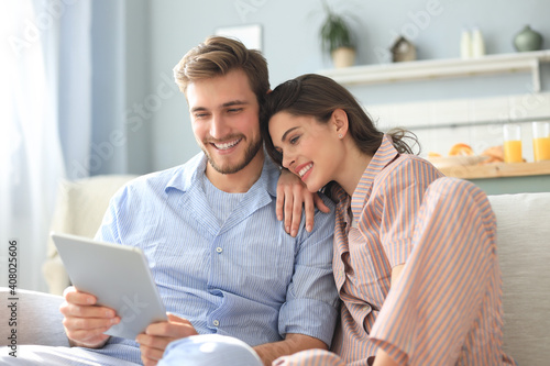 Young couple in pajamas watching media content online in a tablet sitting on a sofa in the living room.