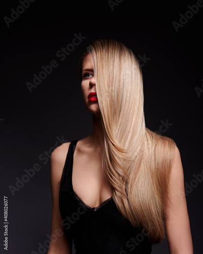 Elegant hairstyle on blond with long hair. Female model with Hollywood hair style. Portrait of woman in black dress with long blond hair.