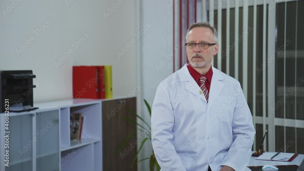Senior male doctor sitting at doctor's table and looking at phone. Thoughtful experienced doctor consults patient via video connection. Senior male doctor sitting at doctor's table and looking at phone. Thoughtful experienced doctor consults patient via video connection.