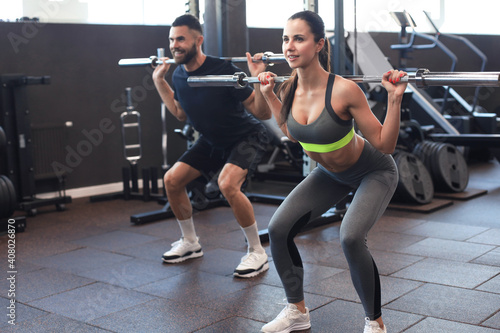 Man and woman with barbell flexing muscles in gym. photo