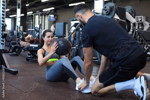 Trainer helping young woman to do abdominal exercises in gym.