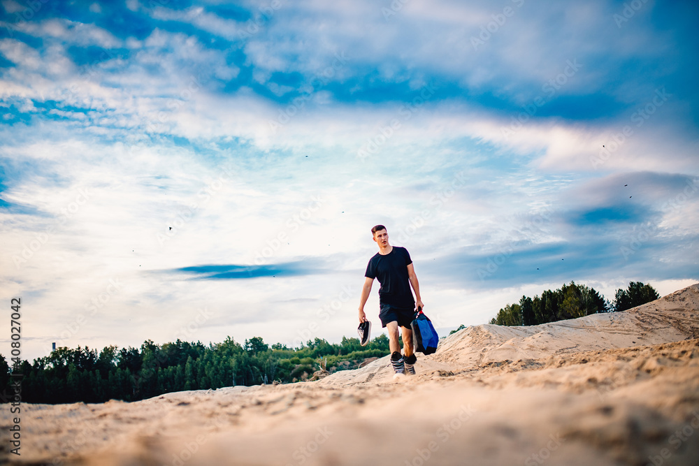 Obraz premium Man carries snowboard equipment for descending on sand in desert. Vacation concept in Arab Emirates and Africa