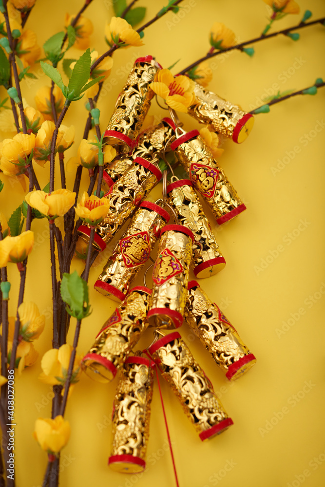 Golden firecrackers with best wishes inscription and blooming apricot branches on yellow table prepared for Tet Lunar New Year