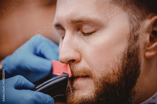 Close-up of barber with medical gloves shearing beard to man in barbershop. Haircut coronavirus pandemic protection