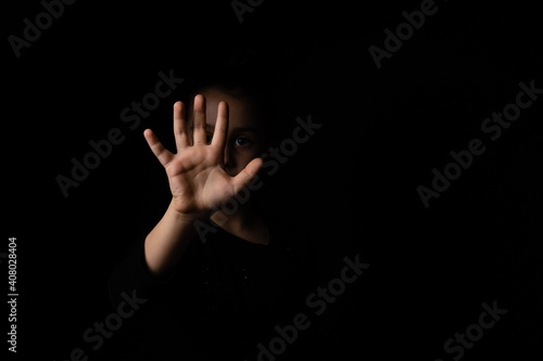 little girl with a raised hand making a stop sign gesture on a black background. Violence, harassment and child abuse prevention concept. photo