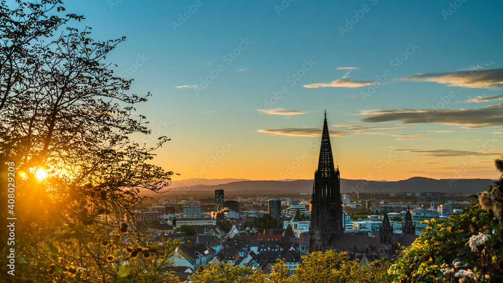 Germany, Freiburg im Breisgau, Magical orange sunset sky and sunrays behind skyline of the beautiful city and muenster