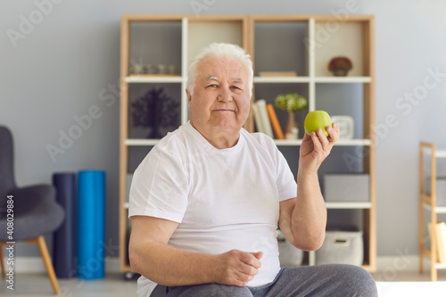 Portrait of an elderly man sitting on a chair with a green fresh apple in his hand.
