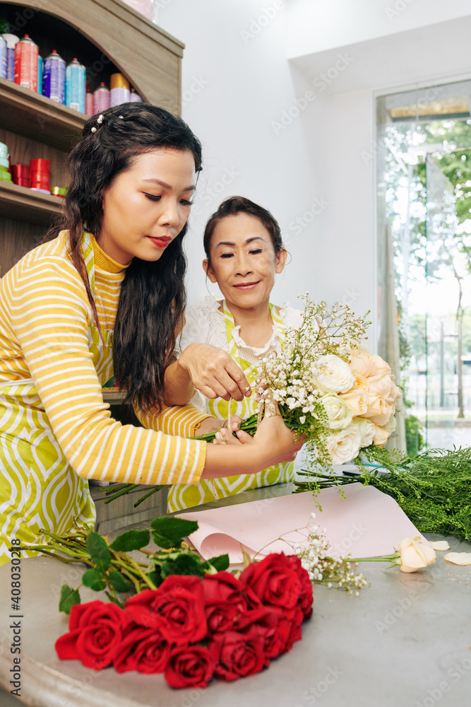 Smiling experienced florist helping new worker to make her first bouquet