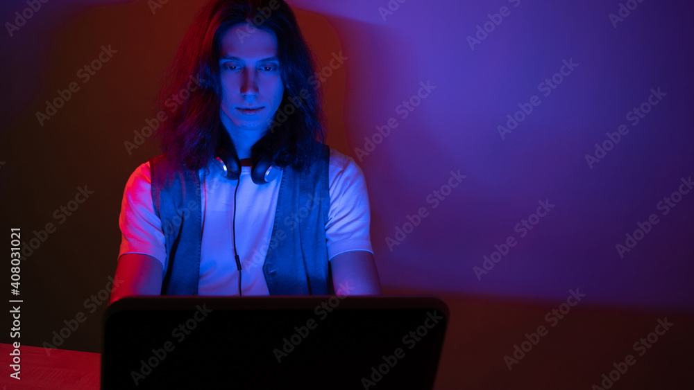 geek guy is learning new technologies, programming, and computer modeling. The student studies programming languages, e-learning. A young man with long hair is working on a laptop. geek guy is learning new technologies, programming, and computer modeling. The student studies programming languages, e-learning. A young man with long hair is working on a laptop.