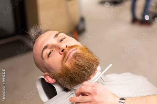 European brutal man with a beard cut in a barbershop