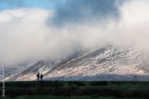 Epic landscape image of Skiddaw snow capped mountain range in Lake District in Winter with low level cloud around peaks viewed from Derwentwater photo