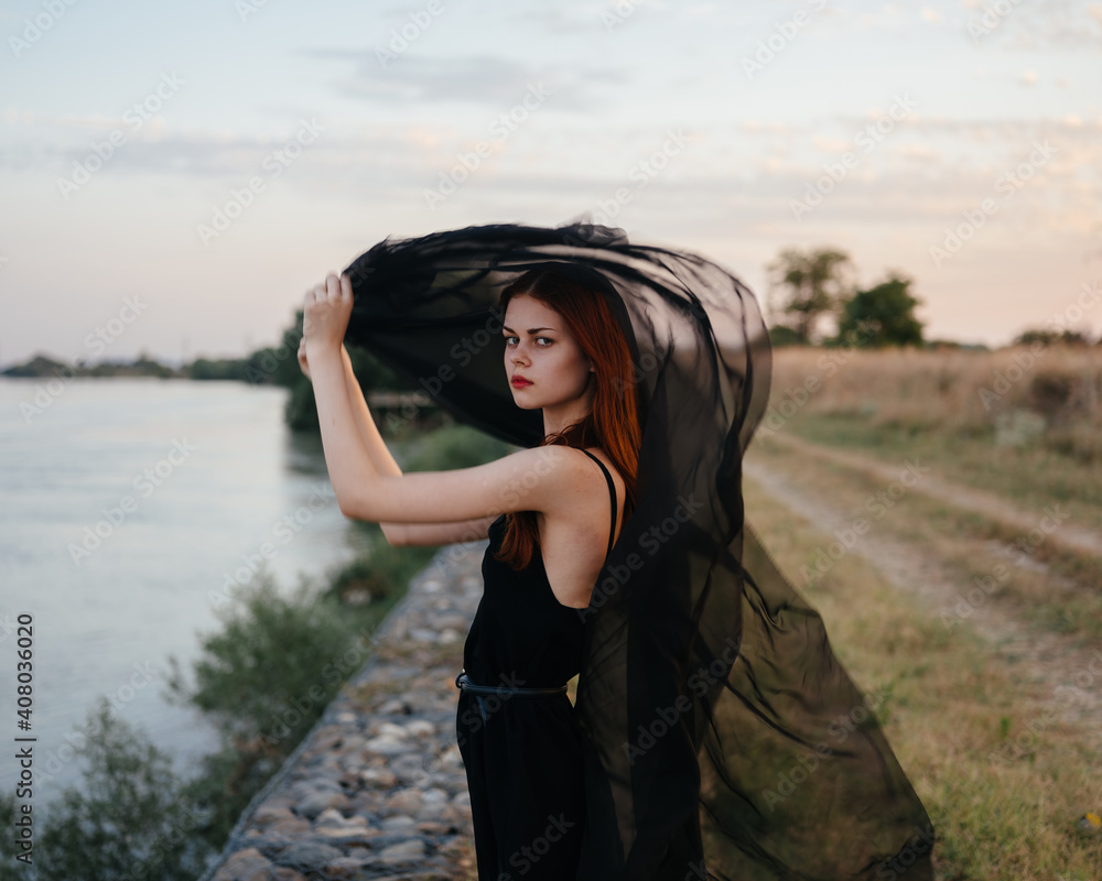 A woman in a dress with a black scarf outdoors near the river