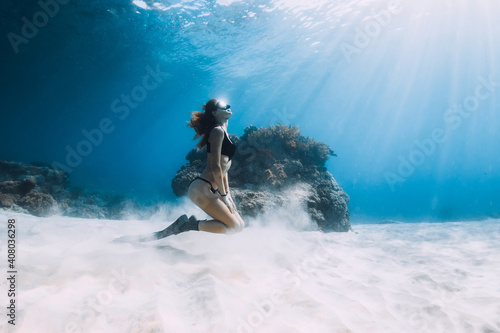 Freediver slim woman with fins posing over sandy bottom underwater sea