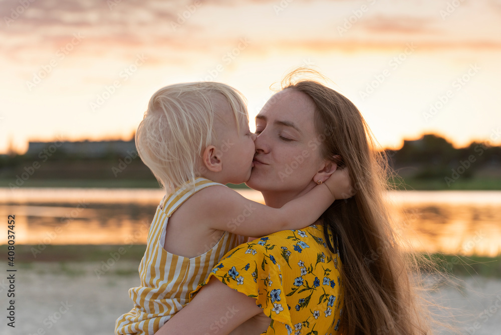 Mother holding baby and gently kisses him. Mother and child in nature at sunset Mother holding baby and gently kisses him. Mother and child in nature at sunset