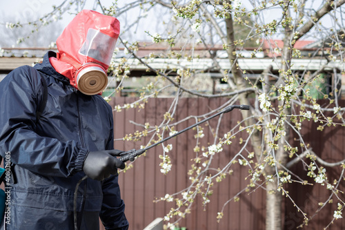 man in protective clothing in the backyard using hand sprayer with pesticides. Pest control. selective focus