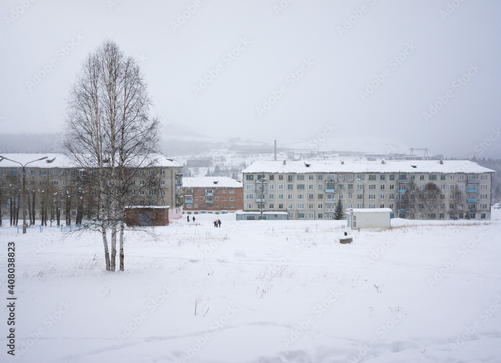 Residential buildings during a snowfall in the working village of Belogorsk against the background of mining industrial buildings. Kemerovo region. Russia.