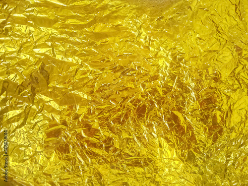Shiny gold foil texture background. Sheet of golden paper. Pattern of yellow wrapping paper with wrinkles and folds. Rich vibrant decorative texture