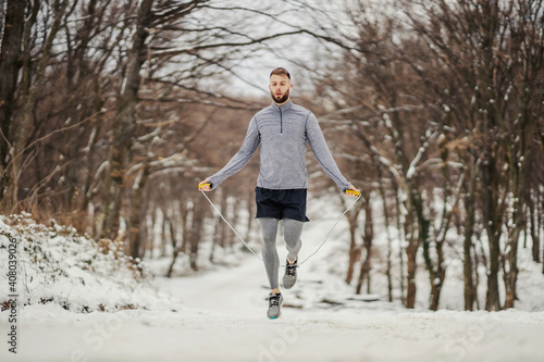 Sportsman in shape jumping rope in nature on snow at winter. Winter fitness, healthy habits, chilly weather