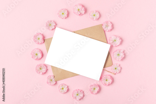 Blank greeting card in frame made of pink cherry blossoming flowers on pastel pink background. Flat lay. Mock up