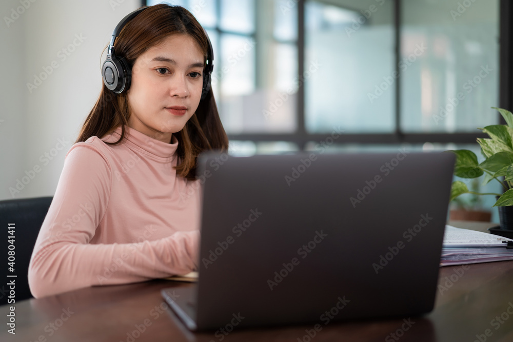Smiling Asian girl student wears wireless headphones write on the notebook to study language online watch and listen to the lecturer, webinar via video call e-learning at home, distance education Smiling Asian girl student wears wireless headphones write on the notebook to study language online watch and listen to the lecturer, webinar via video call e-learning at home, distance education